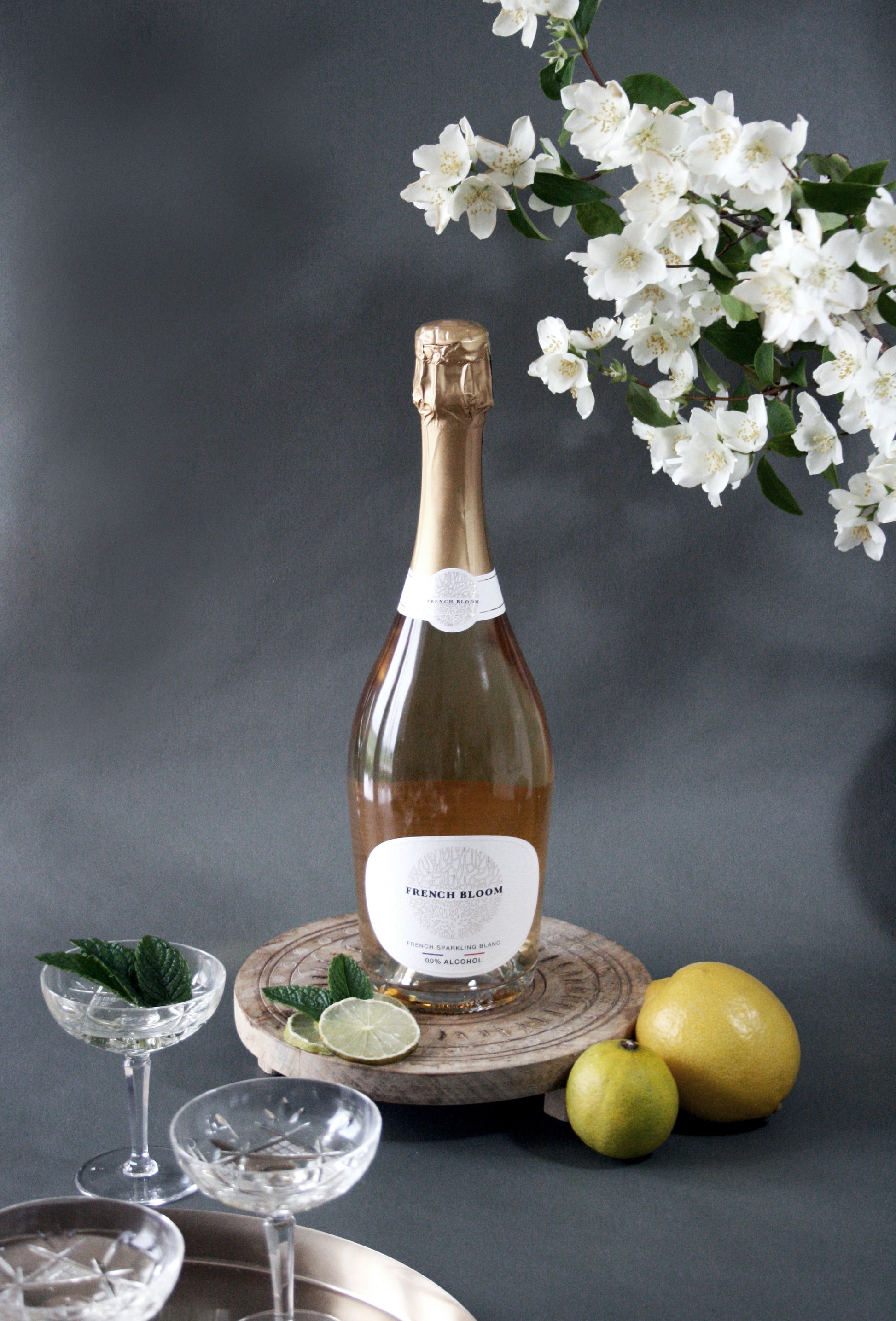Bottle of champagne on a wooden coaster with fruit and glasses on a dark background
