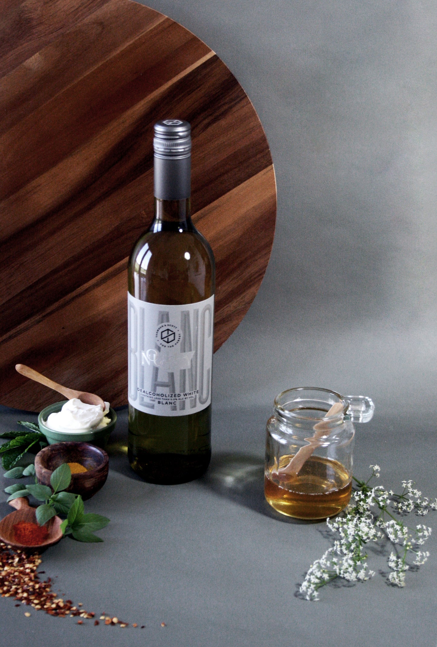 Bottle of wine with a label, glass mug with honey, and small bowls on a gray surface.