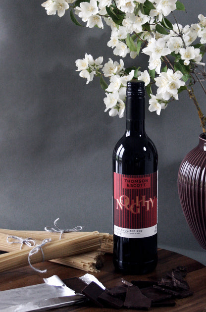 Wine bottle with a red label on a wooden table with white flowers in the background